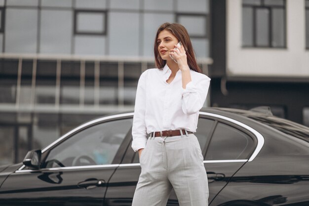 Business woman standing by the car and using phone