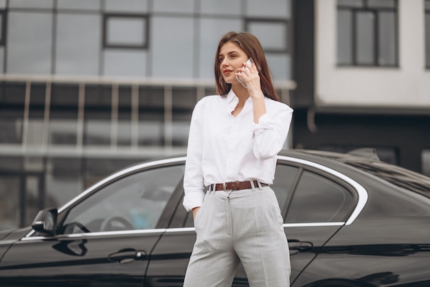 Деловая женщина, стоя у машины и с помощью телефона