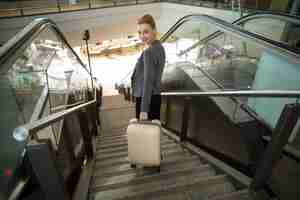 Free photo business woman standing on escalator with luggage