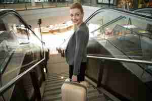 Free photo business woman standing on escalator with luggage