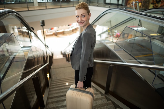 Business woman standing on escalator with luggage