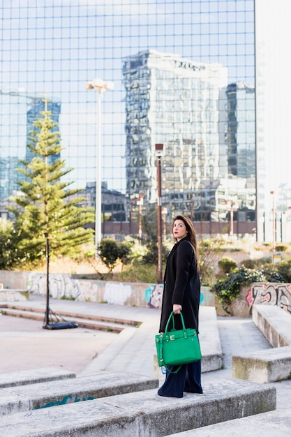 Free photo business woman standing with green bag outside