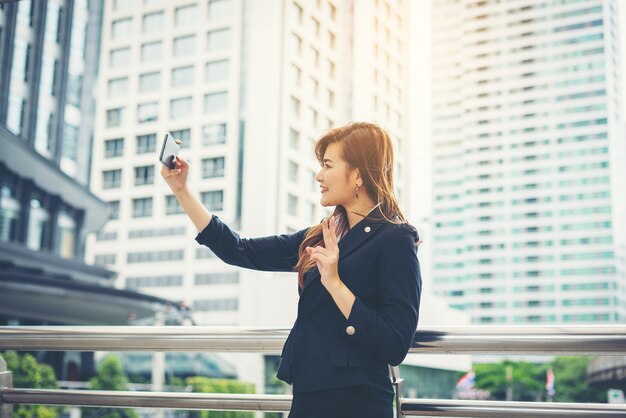 Деловая женщина, взяв selfie на телефоне в передней части офисного здания.