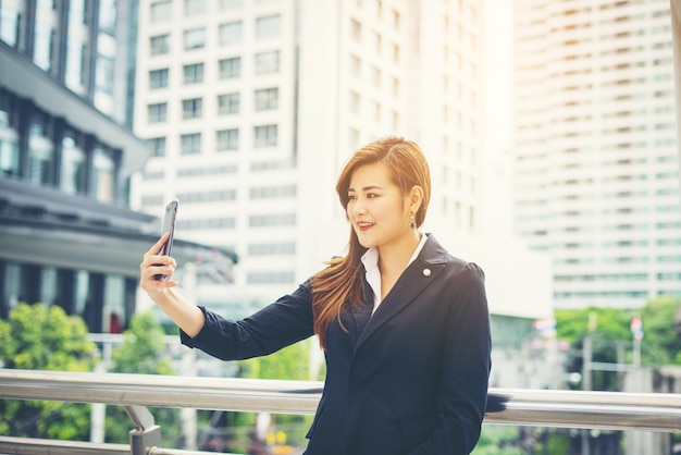 Business woman taking selfie on the phone in front of office building.