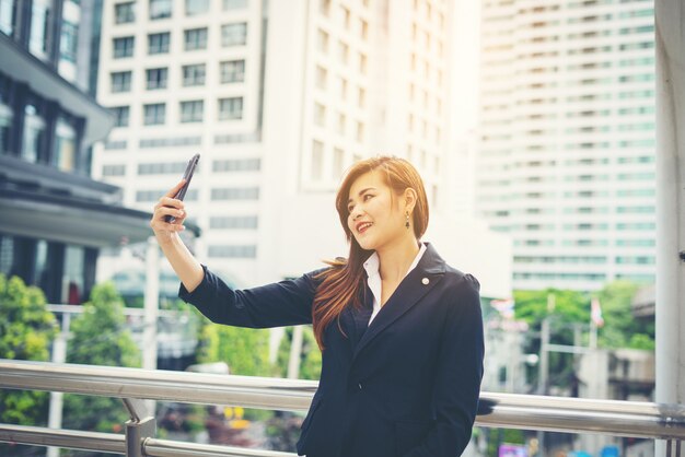 사무실 건물의 앞에 전화 selfie를 복용 비즈니스 여자.