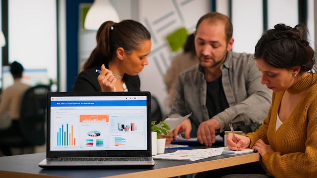 Business woman talking about financial project, taking notes, discussing start up ideas using laptop. Diverse employees gathered in co-working, working process in busy company, teamwork help concept