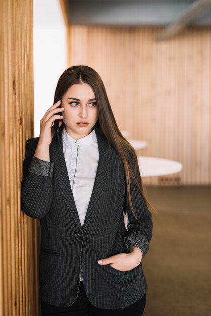 Business woman talking by phone at wall