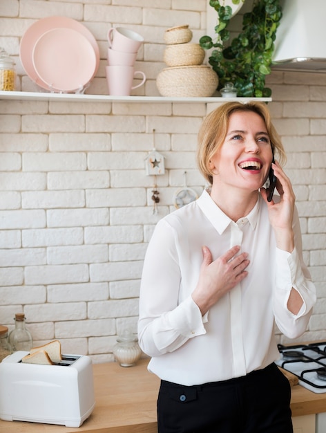 Business woman talking on phone and laughing in kitchen 