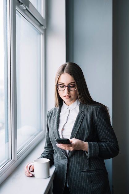 Business woman using smartphone at window 