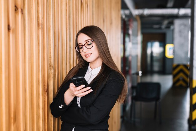 Business woman using smartphone at wooden wall