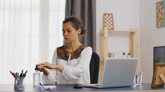 Business woman washing her hands with sanitizer while working from home.