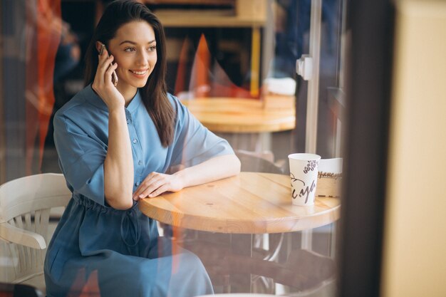 Donna d'affari con caffè e parlando al telefono in un caffè