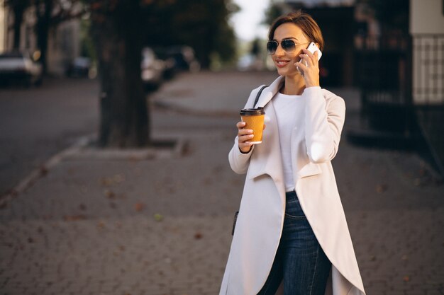 Business woman with phone drinking coffee outside in street