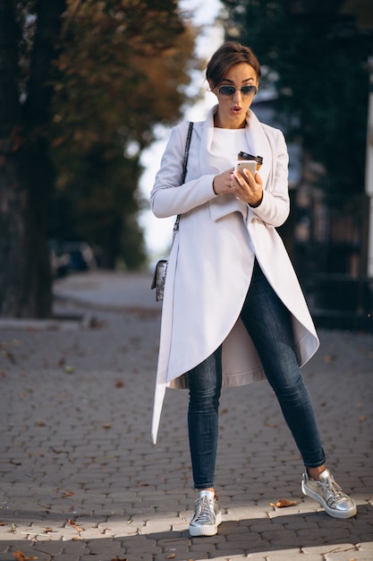 Business woman with phone drinking coffee outside in street