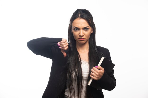 Business woman with thumb down holding clipboard on white wall