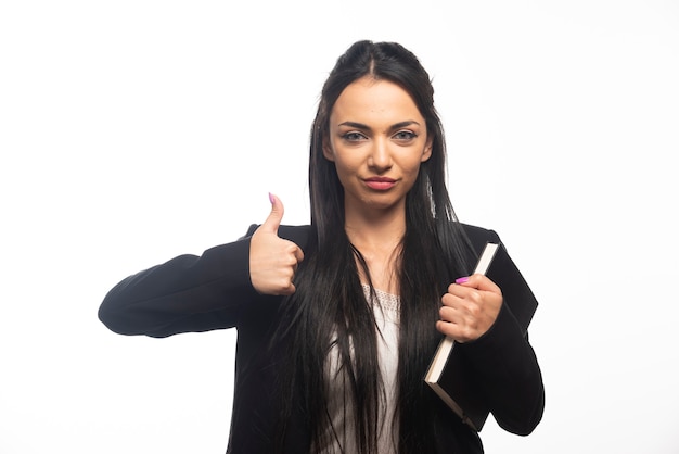 Business woman with thumb up holding clipboard on white wall