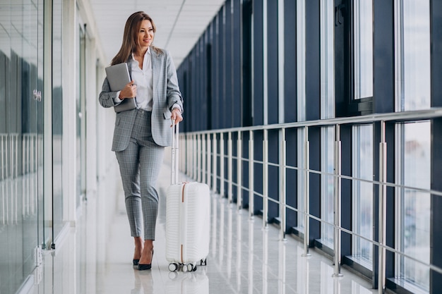 Business woman with travel luggage in airport, holding laptop