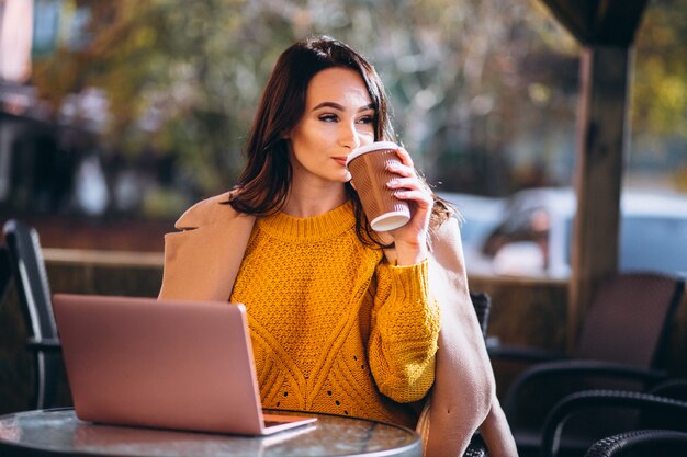 ビジネスの女性がコンピューターに取り組んでいるとコーヒーを飲む