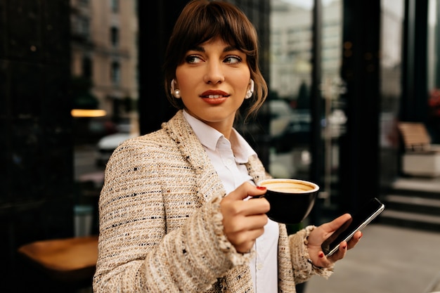 Business woman working with smartphone while drinking coffee outside on city background High quality photo