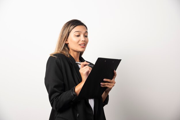 Business woman writing in clipboard on white wall. 