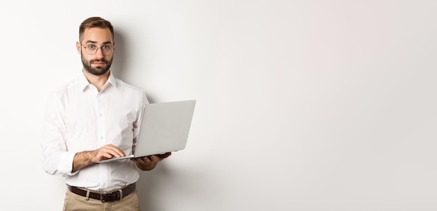 Foto gratuita giovane uomo d'affari bello di affari che lavora al computer portatile facendo il lavoro sul computer che sta sopra la parte posteriore bianca