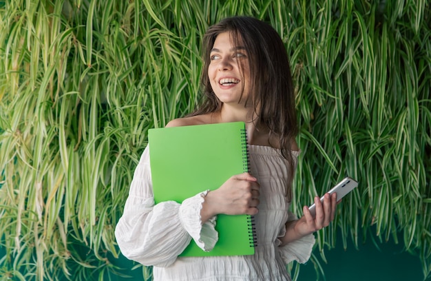 Free photo business young woman with a folder on the background of green plants