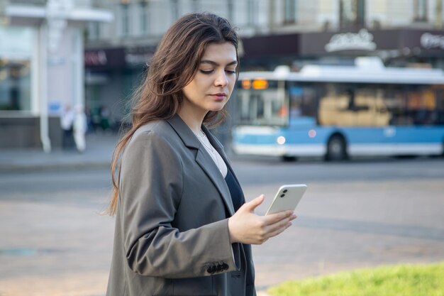 街のぼやけた背景にスマートフォンを持つビジネスの若い女性