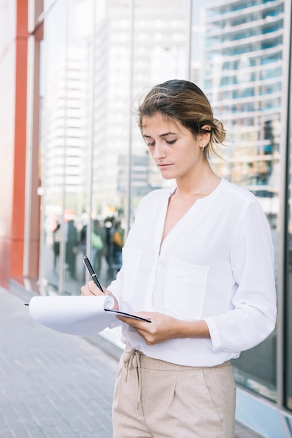 ビジネスの若い女性がペンでクリップボードに書き込む