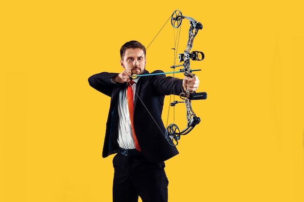 Бесплатное фото Бизнесмен, направленный на цель с луком и стрелами, изолированные на желтом фоне студии. бизнес, цель, вызов, конкуренция, концепция достижения