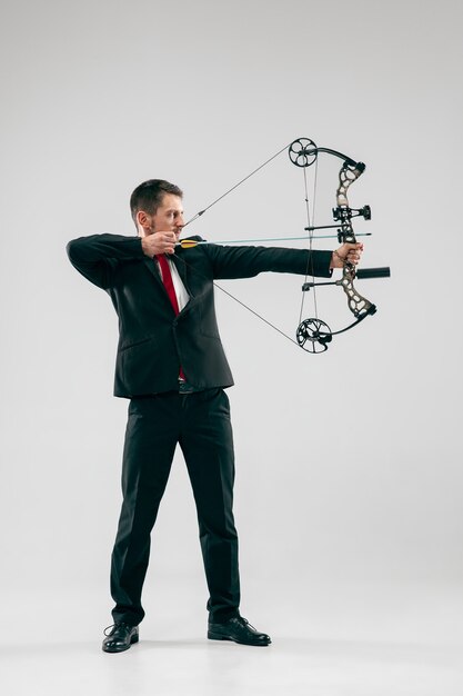 Businessman aiming at target with bow and arrow, isolated on gray background.