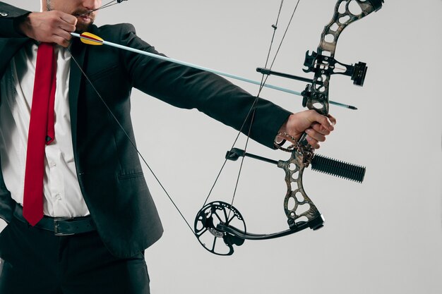 Бизнесмен, направленный на цель с луком и стрелами, изолированные на сером фоне.