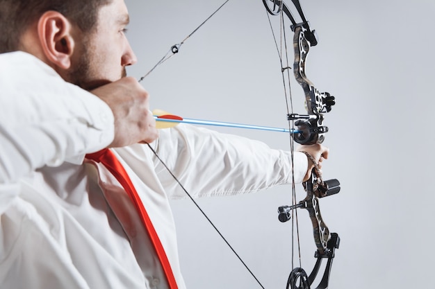 Businessman aiming at target with bow and arrow, isolated on gray studio background. The business, goal, challenge, competition, achievement concept