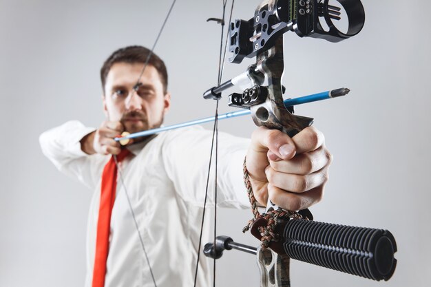 Businessman aiming at target with bow and arrow, isolated on gray studio background. The business, goal, challenge, competition, achievement concept