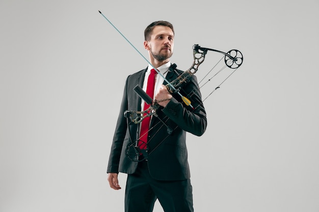 Free photo businessman aiming at target with bow and arrow isolated on gray studio background. the business, goal, challenge, competition, achievement, purpose, victory, win, clarity, winner and success concept