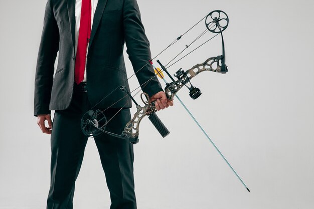 Businessman aiming at target with bow and arrow isolated on gray studio background. The business, goal, challenge, competition, achievement, purpose, victory, win, clarity, winner and success concept