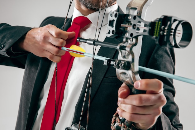 Businessman aiming at target with bow and arrow isolated on gray studio background. The business, goal, challenge, competition, achievement, purpose, victory, win, clarity, winner and success concept