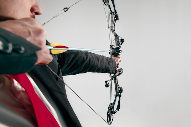 Businessman aiming at target with bow and arrow isolated on gray studio background.