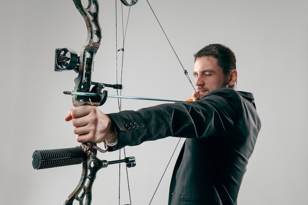 Businessman aiming at target with bow and arrow isolated on gray studio background.
