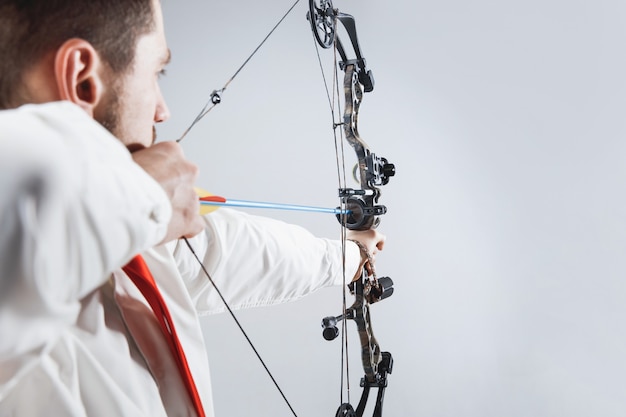 Businessman aiming at target with bow and arrow, isolated on gray studio background.