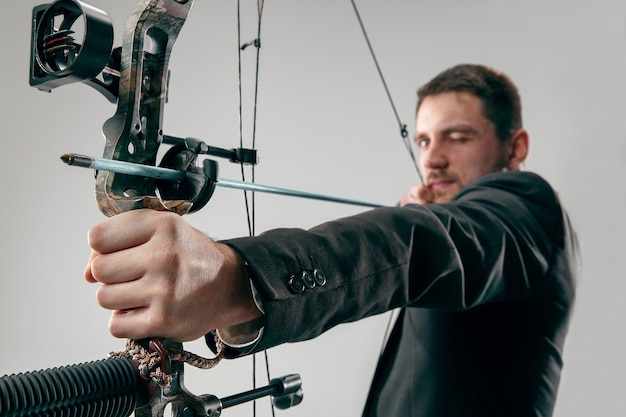 Businessman aiming at target with bow and arrow isolated on gray studio wall