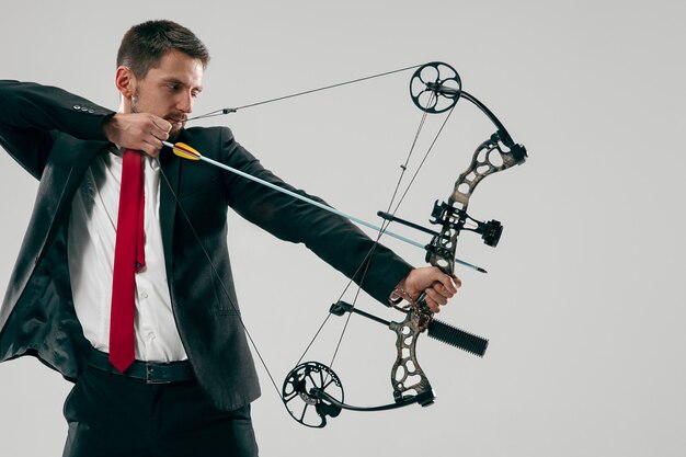 Бизнесмен, направленный в цель с луком и стрелами, изолированный на серой стене студии