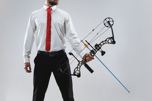 Free photo businessman aiming at target with bow and arrow, isolated on gray studio wall