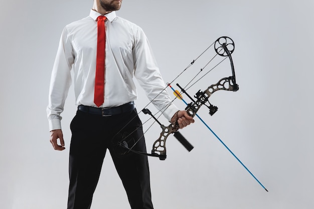 Businessman aiming at target with bow and arrow, isolated on gray studio wall