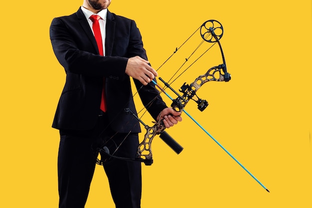 Бизнесмен, направленный на цель с луком и стрелами, изолированные на желтом фоне студии. Бизнес, цель, вызов, конкуренция, концепция достижения