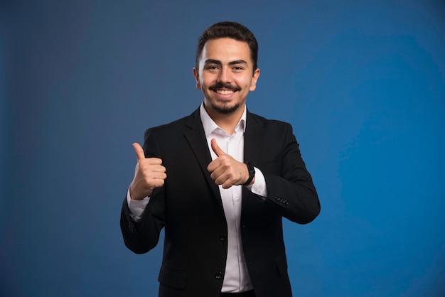 Businessman in black suit makes thumbs up. 