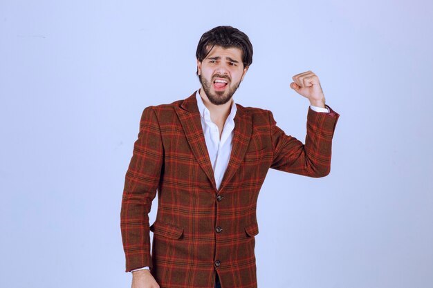 Businessman in brown jacket showing his fists and making point to his success and power.