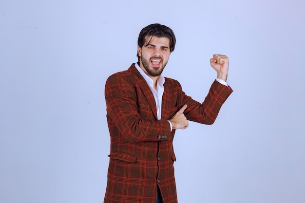 Businessman in brown jacket showing his fists and making point to his success and power.