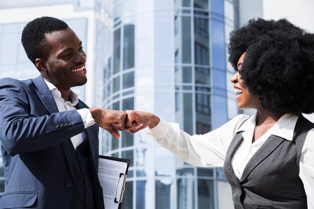 Businessman and businesswoman bumping their fist in front of corporate building