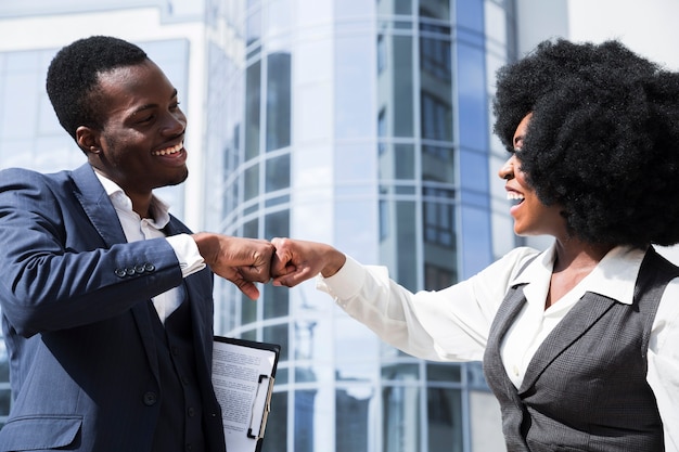 Businessman and businesswoman bumping their fist in front of corporate building