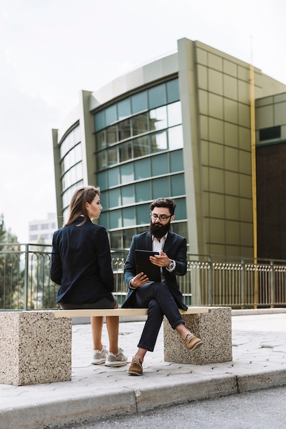 Businessman and businesswoman sitting on bench in front of office building